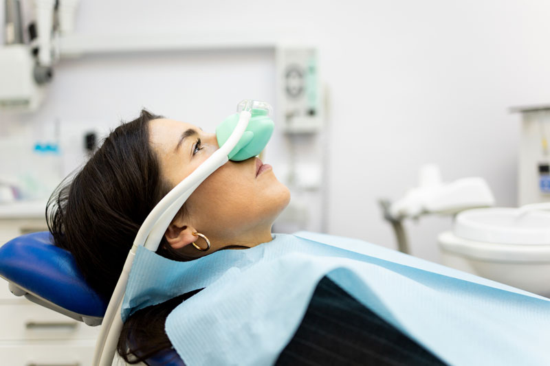 An adult woman sits in a dentist's office wearing a nasal mask to inhale nitrous oxide. Dentist fear concept. Feeling of relaxation with laughing gas.